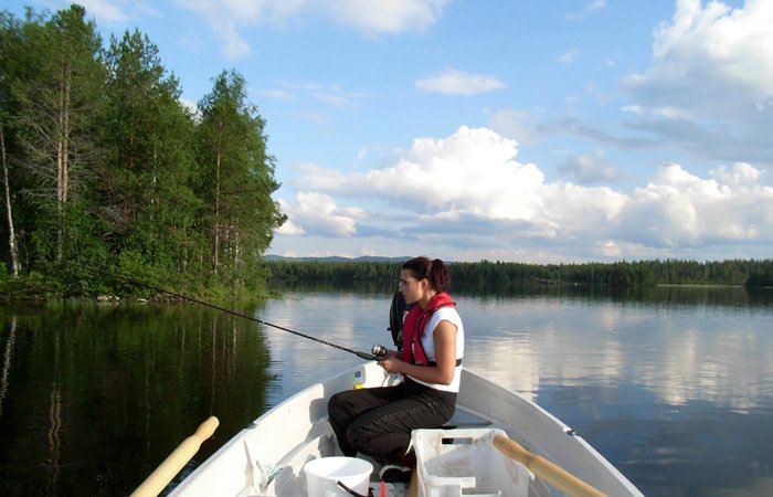 A woman in a life vest sits in a small boat on the Kasilof River, holding a fishing rod as part of the lodge amenities.